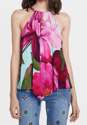 Woman wearing a halter top with large pink floral print paired with light blue jeans embroidered with small colorful floral patterns.