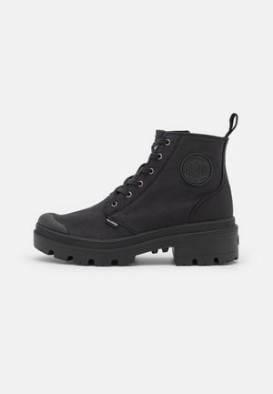 Black canvas ankle boots with a rubber toe cap, textured sole, metal eyelets, and a logo patch on the side. Lace-up design.
