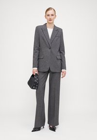 Abito grigio su misura con blazer a un bottone e pantaloni a gamba larga. Abbinato a una borsa nera con hardware in argento e scarpe a punta.