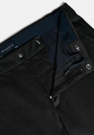 Zwarte broek met een soepele textuur, voorzien van een ritssluiting en knoopsluiting, marineblauwe binnenband en merketiket aan de binnenkant.