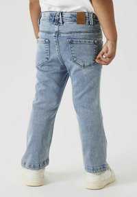 Pantalons en denim bleu clair à jambes droites, poches arrière et étiquette en cuir marron sur la taille. Portés avec des baskets blanches.