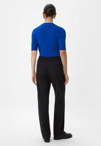 Blauwe kortempelige top van gebreid materiaal, gecombineerd met zwarte, relaxte broek met een elastische tailleband en zijzakken.