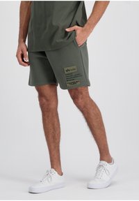 Oliwkowe szorty bawełniane z bocznymi kieszeniami i oliwkową naszywką z napisem. W połączeniu z białymi sneakersami. Gładka tekstura, luźny krój.