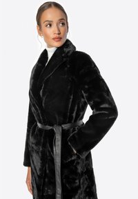 Černý kabát z umělé kožešiny s šálovým límcem, páskem v pase a dlouhými rukávy; má jemnou texturu a elegantní design.