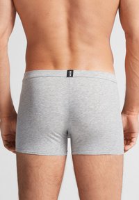 Grå bomullsboxershorts med en åtsittande passform, med en platt midja och slät textur, synlig sömnad längs kanterna.