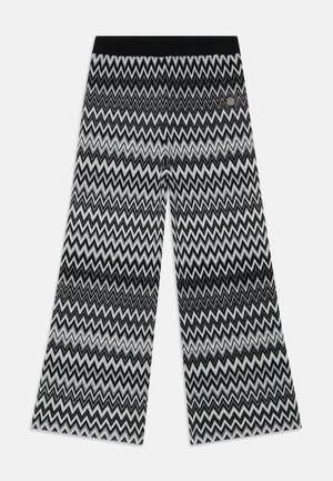 Pantalones de pierna ancha con estampado de chevron en blanco y negro, con una cinturilla sólida negra y un detalle de logo metálico cerca de la cinturilla.