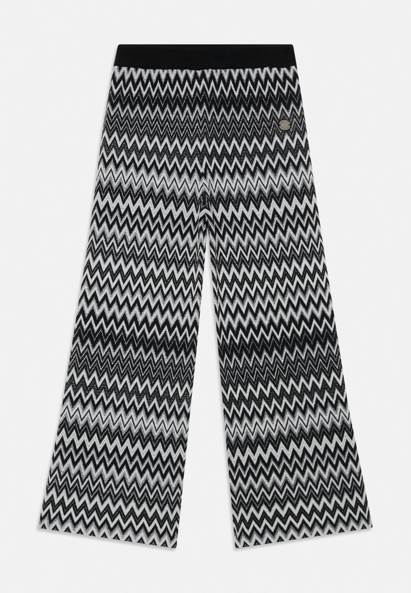 Svartvita byxor med chevron-mönster i vida ben, med en enfärgad svart midja och en metall-logotypdetalj nära midjan.