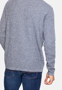 Grauer Strickpullover mit strukturiertem Muster, langen Ärmeln und abgerundetem Saum. Über einer blauen Jeans getragen, zeigt einen lässigen Look.