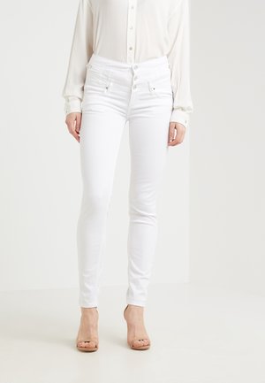 Jeans blancos de tiro alto con un diseño ajustado, que cuentan con múltiples botones y sutiles detalles de costura, combinados con una blusa ligera.