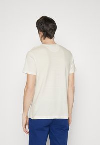 Lys beige kortærmet t-shirt med en diskret ribbet struktur, rund halsudskæring og lige kant, parret med blå bukser.