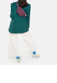 Vihreä bleiseri, ylisuuret valkoiset housut, purppurainen olkalaukku, kevyet raidalliset kengät, siniset sukat ja suorat hiukset, nähtynä takaa.