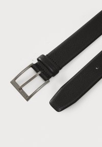 Ceinture en cuir noir avec une finition texturée, dotée d'une boucle rectangulaire en argent et d'une lanière lisse. Comprend un seul trou d'ajustement.