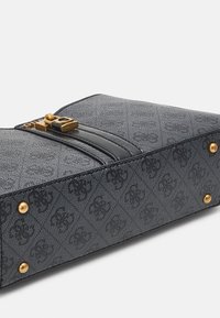 Musta teksturoitu käsilaukku, jossa on kultasävyinen solki, kaksi vaakasuoraa raitaa ja kultaisia niittejä pohjassa. Kompakti suorakulmainen muoto.