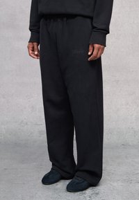 Pantalones de chándal negros con un ajuste relajado, fabricados en una tela suave, que cuentan con un detalle de logotipo bordado y una cintura elástica para mayor comodidad.