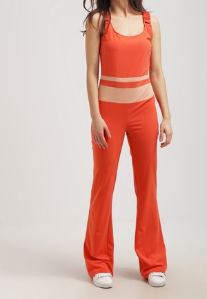 Czerwony kombinezon z szerokimi nogawkami i dopasowanym gładkim stanikiem ozdobionym przezroczystymi paskami. Materiał wygląda na gładki, z paskami zaprojektowanymi dla regulowanego dopasowania.