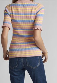 Hedvábný pletený top v růžových, levandulových, modrých a žlutých pruzích. Má krátké volánkové rukávy a přiléhavý střih, v kombinaci s modrými džínami.