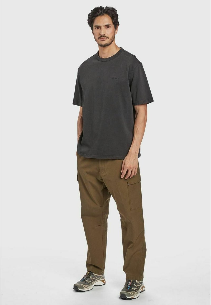 T-shirt in cotone grigio scuro con scollo rotondo, abbinato a pantaloni cargo beige con tasche laterali e vestibilità comoda. Sneakers grigie notevoli.