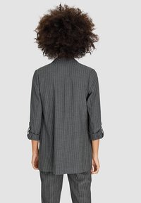 Blazer gris à fines rayures avec manches retroussées aux trois quarts, confectionné dans un tissu léger. Coupe droite avec une texture lisse et un design structuré.