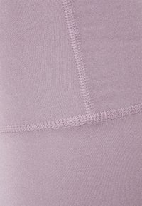 Leggings lilas clairs en tissu lisse et extensible avec des coutures flatlock pour plus de confort. Aucun motif visible ni détail matériel.