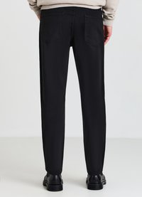 Schwarze gerade Hosen mit zwei Gesäßtaschen, glatter Textur und minimalen Details, kombiniert mit schwarzem Schuhwerk.