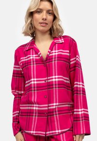 Il pigiama di flanella rosa presenta un grande motivo a quadri con strisce bianche e rosa scuro, maniche lunghe e una chiusura frontale con bottoni.