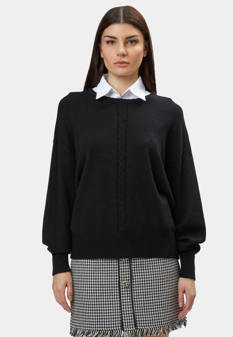 Schwarzer Strickpullover mit rundem Halsausschnitt und Zopfmuster, kombiniert mit einem weißen Hemd mit Kragen. Der Stoff ist weich und die Ärmel sind lang und weit.