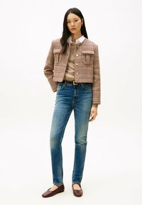 Chaqueta recortada a cuadros en tela roja y beige con dos bolsillos frontales, combinada con un suéter beige, jeans azules y zapatos planos color burdeos.
