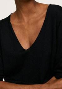 Pull noir avec un décolleté en V prononcé, texture côtelée douce et manches amples, présentant un design minimal et un style contemporain.