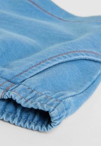 Ljusblå denimtyg med elastisk fåll, med synlig orange sömnad och en mjuk textur. Den böjda formen framhäver tygets fall.