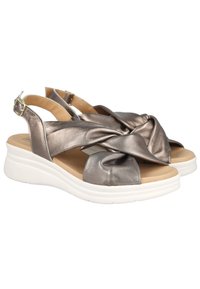 Sandalias de bronce metálico con diseño retorcido, punta abierta y correa ajustable en el talón, con suela de plataforma blanca.