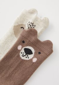 Braune und cremefarbene Socken mit Bärenmotiven; weiches Strickmaterial, runde Oberseiten und Gesichtsdetails mit schwarzen, rosa und braunen Akzenten.