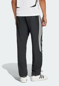 Svarta träningsbyxor av lättviktig tyg, med vita sidostrippar och en avsmalnande passform, tillsammans med vita sneakers.