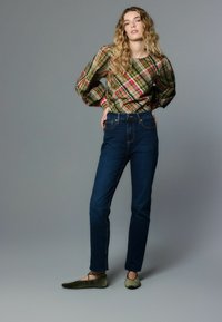 Grün-rosa karierte Bluse mit Puffärmeln, kombiniert mit dunkelblauen Jeans und olivgrünen Ballerinas, mit figurbetontem Schnitt und klassischer Nahtführung.