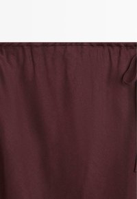 Close-up af vinrødt stof med syet øverste kant og en stofløkke på højre side.