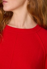 Maglione a coste rosso, con collo alto, maniche raglan e una vestibilità rilassata. Tessuto liscio con una cucitura frontale.