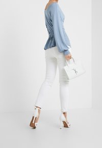 Haut bleu clair à manches longues avec un dos froncé, associé à un jean blanc et des sandales à talons blanches. Accompagné d'un sac à main structuré blanc.