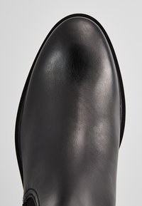 Zapato de piel negra con una superficie lisa y pulida y punta redondeada. Presenta un diseño sin costuras y acentos mínimos, resaltando su silueta elegante.