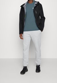 Černá lehká bunda přes tyrkysové tričko, doplněná o šedé tepláky a černé boty. Hladká tkanina s přiléhavým střihem.