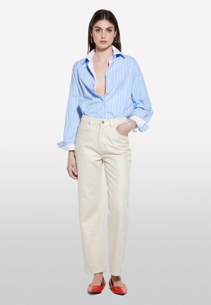 Hellblau gestreifte Bluse mit hochgerollten Ärmeln, kombiniert mit crèmefarbenen Hosen und roten Ballerinas. Fokus auf lässigem, entspanntem Schnitt und Textur.