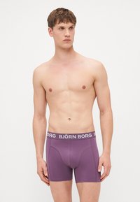Purple boxer briefs with a white "BJÖRN BORG" logo waistband. Smooth fabric, fitted shape, and mid-thigh length.