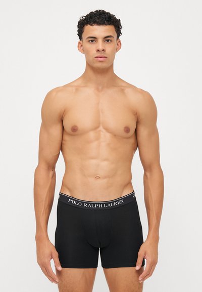 Črne bokserice brez šivov z elastičnim pasom, na katerem je v beli barvi napisan tekst "POLO RALPH LAUREN". Raztegljiv material.