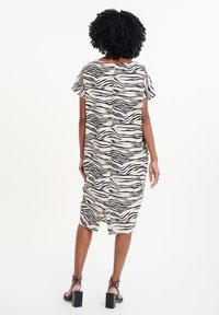 Vestido de rayas de cebra en blanco y negro, con mangas cortas, corte relajado, hasta la rodilla, con un dobladillo redondeado y aberturas en los laterales. Textura de tela suave.