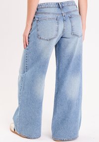 Un jean large bleu clair avec une texture délavée, présentant une taille haute, deux poches arrière et des finitions de couture nettes.