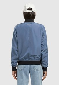 Modrá bomber bunda s elastickým pásom a manžetami. Hladká textúra, minimalistický dizajn, obsahuje čierny golier a detail loga na chrbte.