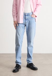 Lys blå jeans med rett passform, denimmateriale, kontrasterende sømmer og frontlommer. Kombinert med en rosa skjorte med knapper og svarte sko.