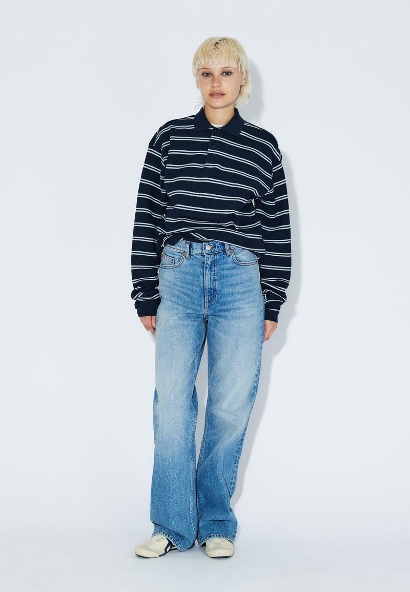 Navy striped long-sleeve polo shirt paired with light blue high-waisted jeans, featuring a relaxed fit and wide leg, worn with cream shoes.