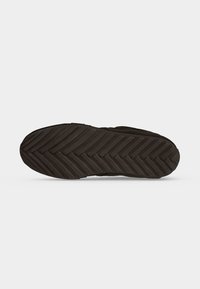 Semelle de chaussure avec bande de roulement en caoutchouc noir présentant des rainures diagonales en chevrons pour l'adhérence et la traction sur surfaces planes.