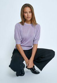 Lila stickad tröja med korta puffärmar och ribbat halsband, matchad med svarta vida byxor och svarta glänsande skor.