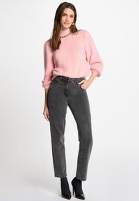 Roze donzige trui met een hoge hals en poffende mouwen, gecombineerd met hoge zwarte jeans en zwarte puntige hakken.