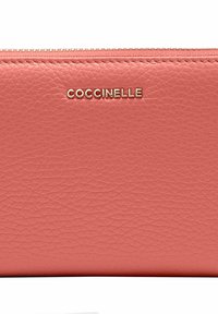 Portafoglio in pelle corallo con finitura testurizzata, logo dorato "Coccinelle" e chiusura con zip lungo il bordo superiore.
